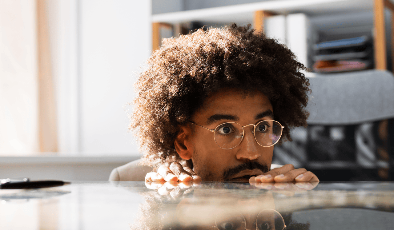 Man wearing glasses, hiding behind desk