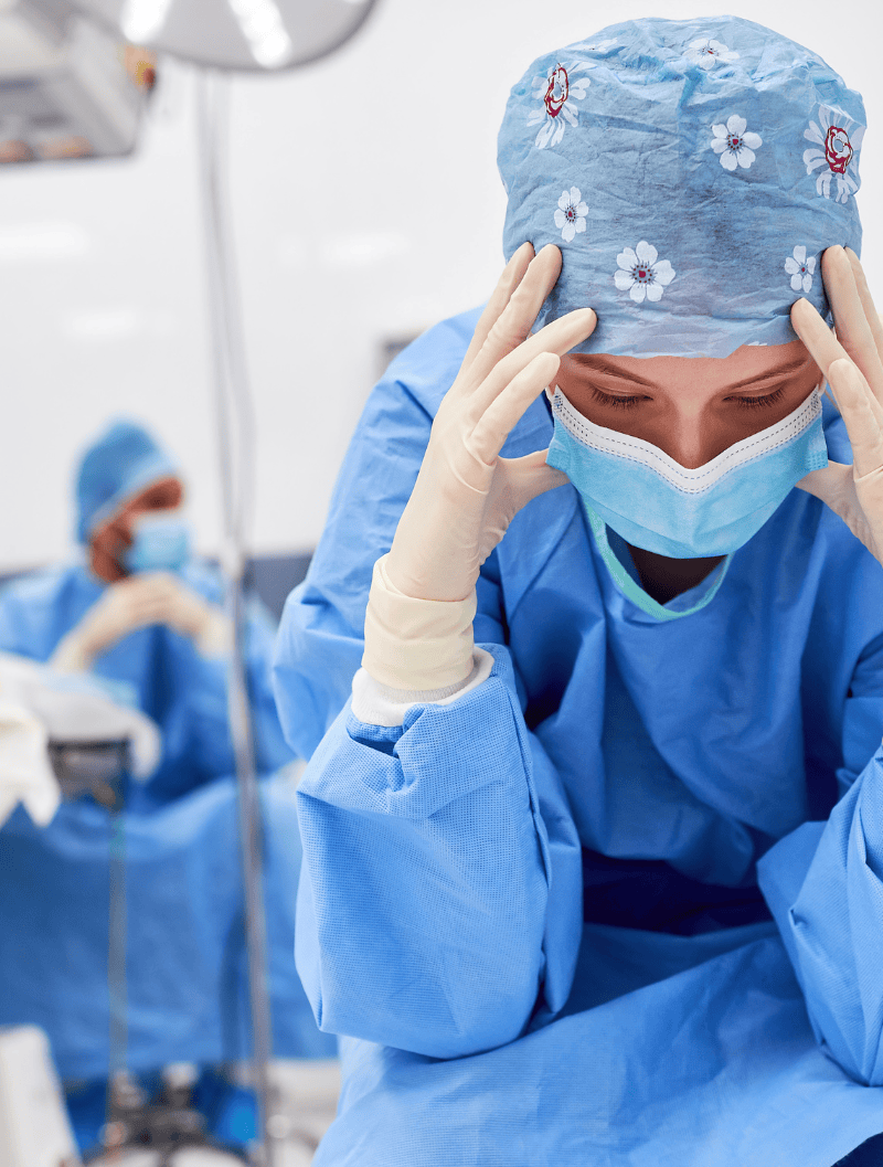 Doctor in scrubs, hands on temples, looking resigned and exhausted.