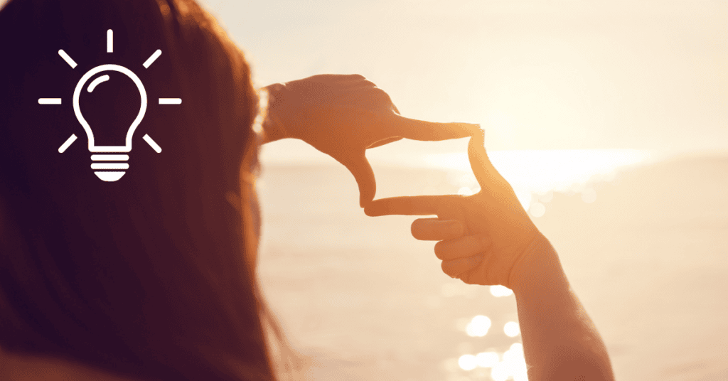 Woman with long reddish hair, facing sunset, looking to the horizon over the ocean, positioning her hands like a square window and looking through to the future.